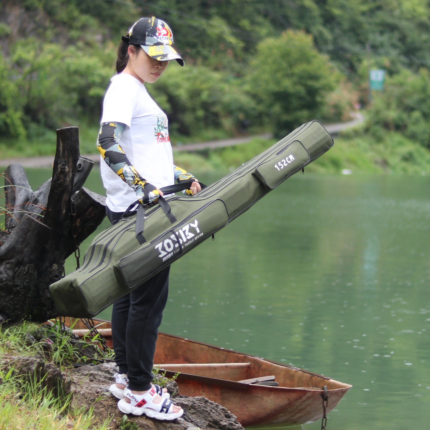 Person holding a green fishing rod case by a lake